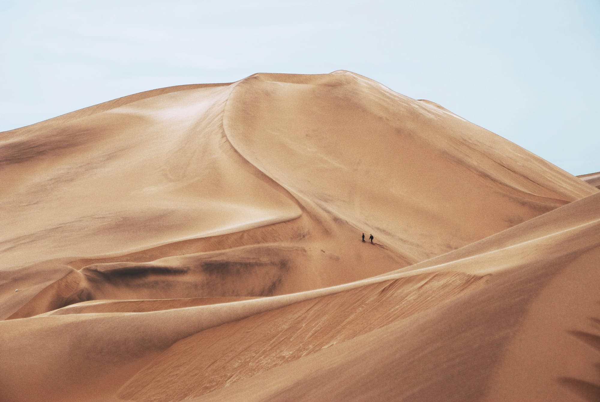 A huge sand dune with people walking in distance